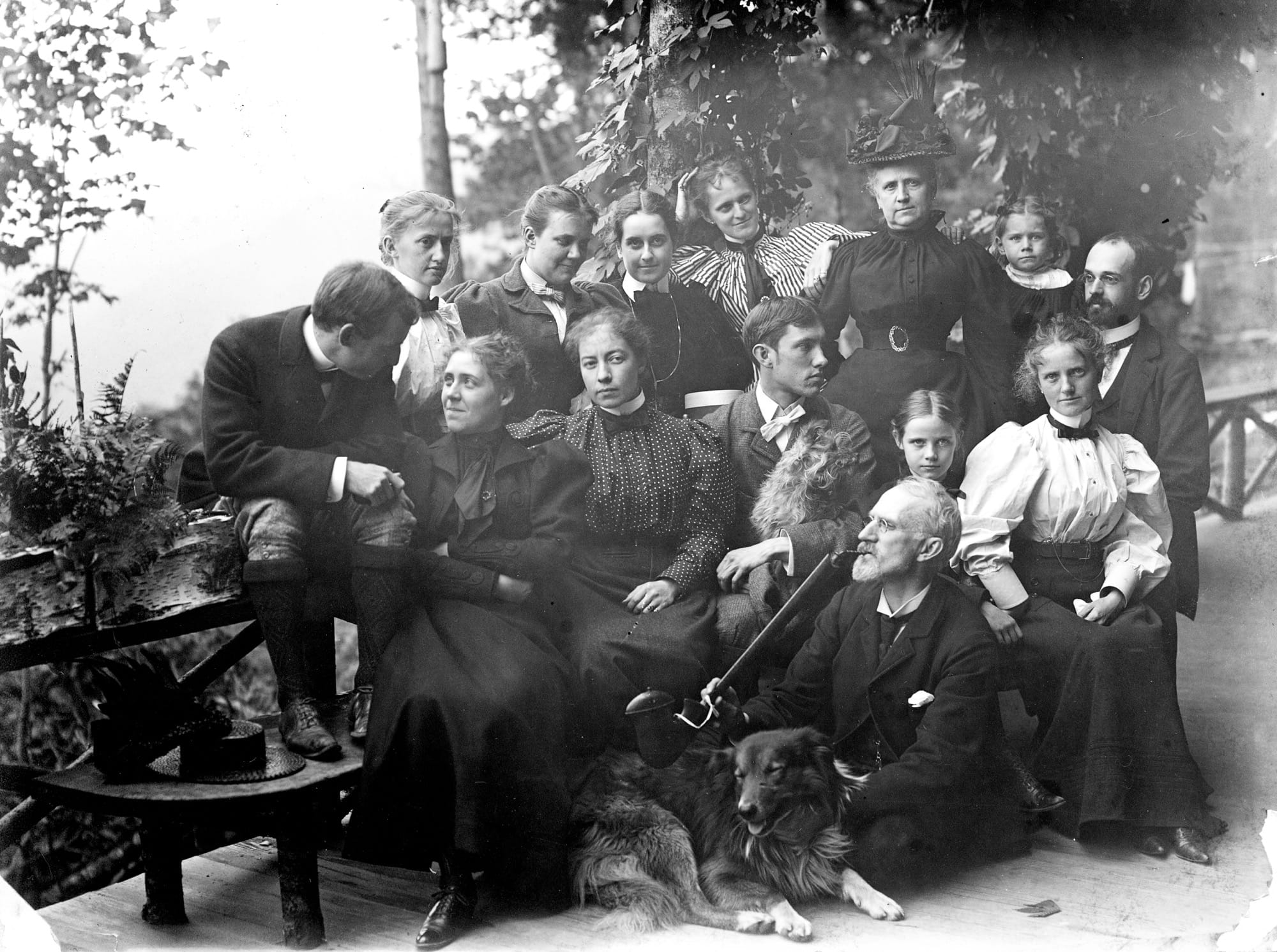 a black-and-white photo from the late 19th century of a large group of friends outside on a veranda