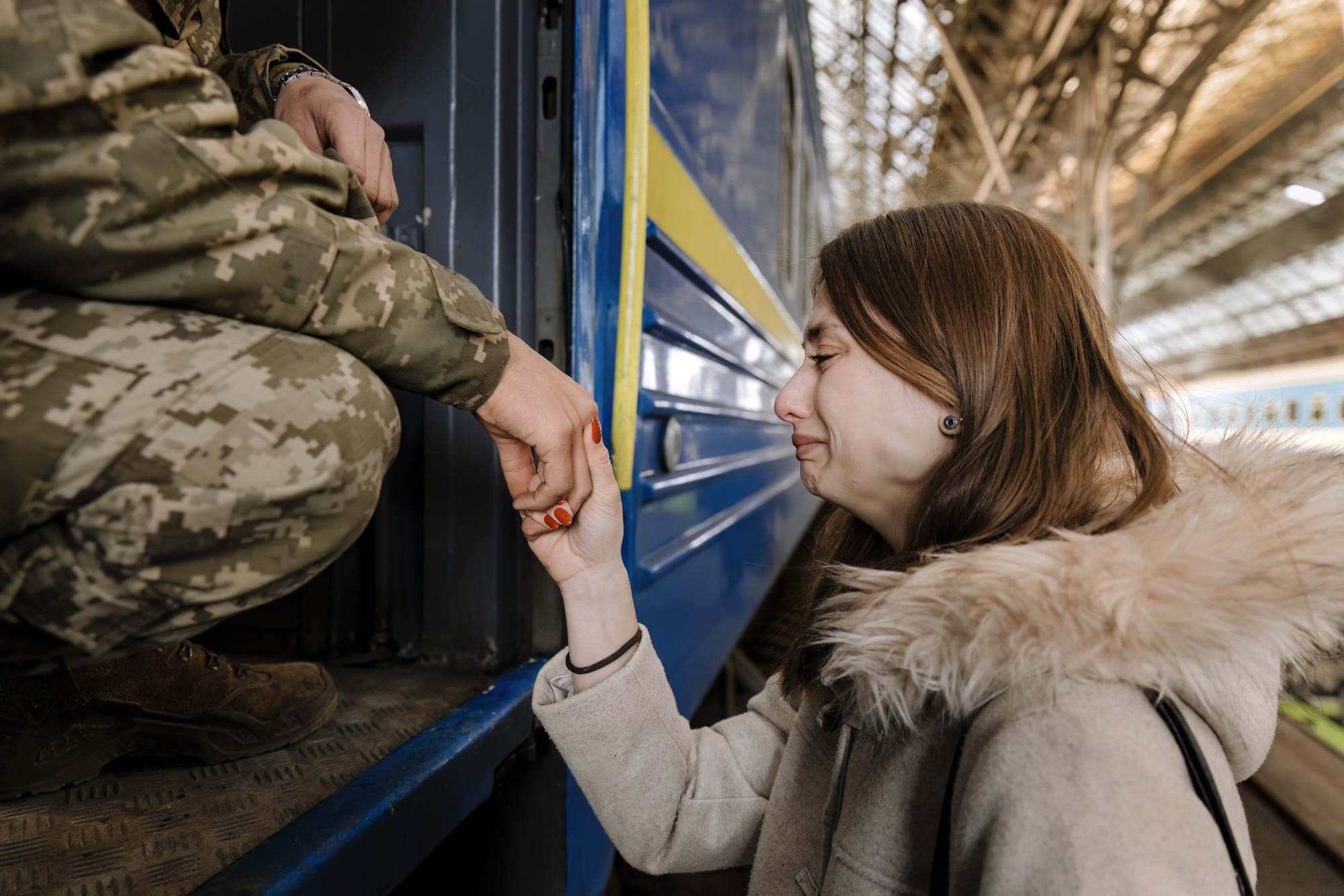 a photo by Ilvy Nijokiktijen of a young woman crying while she holds the hand of a soldier on a train